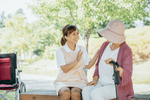 ベンチに座って話す高齢女性と女性介護士