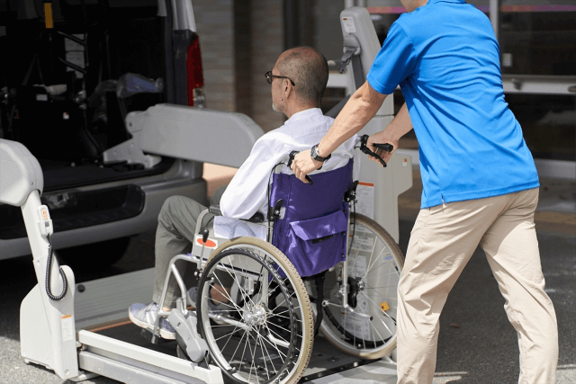 車椅子に乗った高齢者を介護車に載せる男性介護士