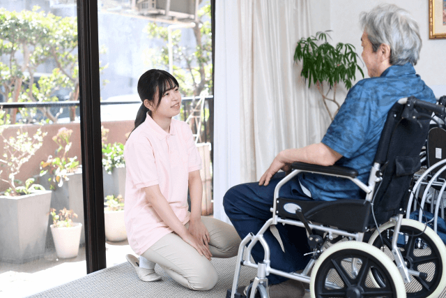 車椅子に座った高齢男性と会話する女性介護士