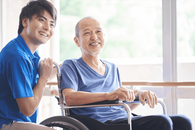 笑顔の男性介護士と車椅子に座っている高齢男性