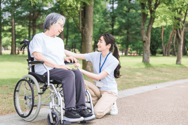 車椅子に座っている高齢女性と跪いて笑顔の女性介護士