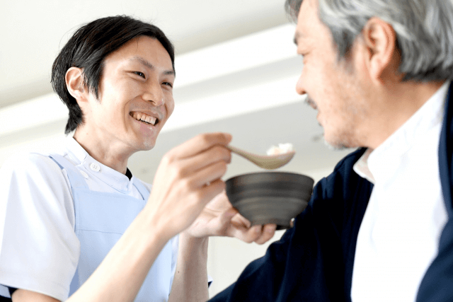 高齢男性の食事をサポートする男性介護士